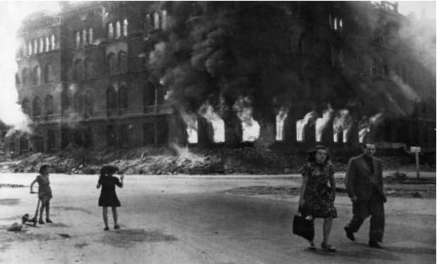 Gli edifici in fiamme fanno parte del normale paesaggio nella Berlino del 1945,  nei pressi della Alexanderplatz due bambini giocano e una coppia passeggia